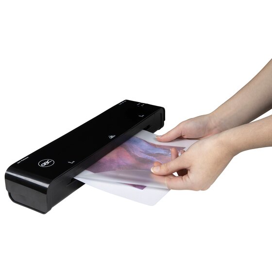 Hands feeding a laminated picture into a black GBC pouch laminator, shown to illustrate use; the laminator is sold separately