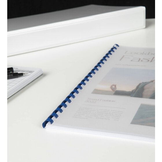 Lookbook booklet with a fashion photo cover bound with a blue plastic comb, on a white desk beside a white binder