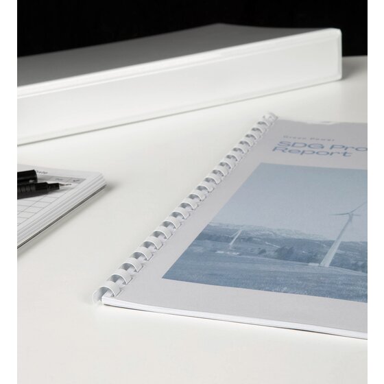 A4 report bound along its edge with a white plastic comb, lying on a white desk in front of a white ring binder and pens