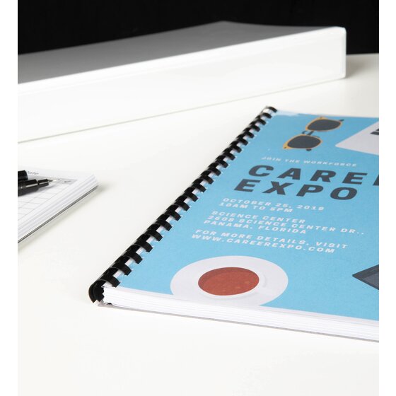 Careers expo document finished with a black plastic binding comb, lying on a white table with pens and a notepad beside it