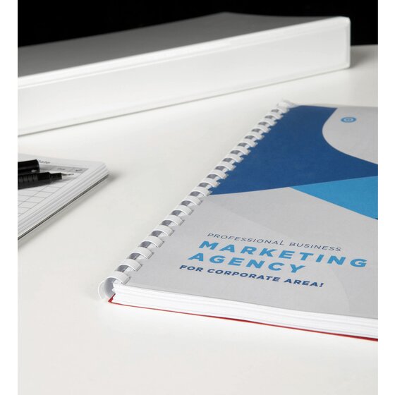 Marketing agency report bound with a white plastic comb, lying on a white desk next to a notepad and pens