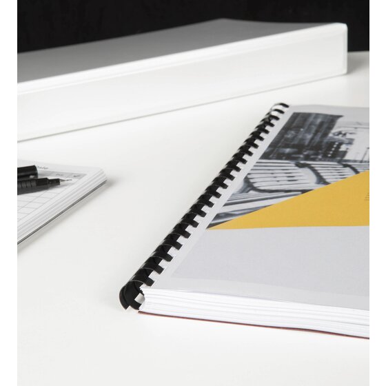 Bound report with a black GBC plastic comb spine lying on a white table, a white folder and pens in the background