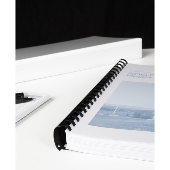 Thick report with a landscape photo on its cover bound with a black GBC plastic comb, on a white desk next to a white binder
