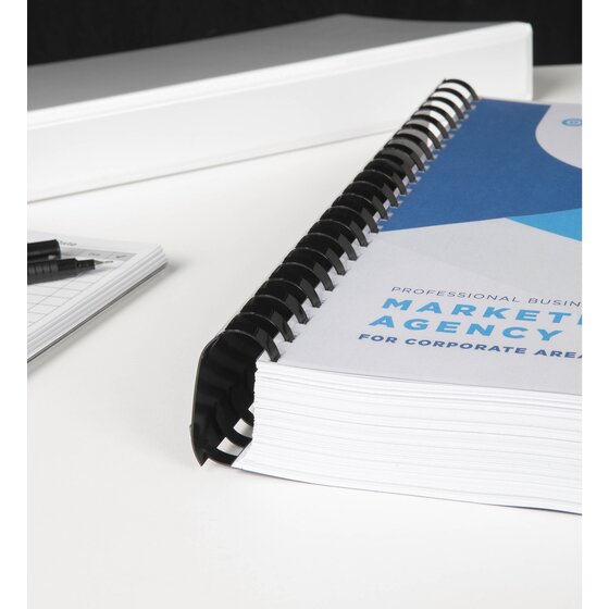 Very thick Marketing Agency book bound with a black GBC plastic comb, lying on a white desk beside a white binder