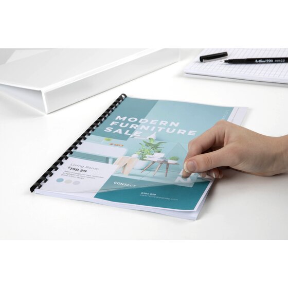 Clear front cover lifted by hand on a furniture sale catalogue bound with a black plastic comb, with a pen and pad in the background