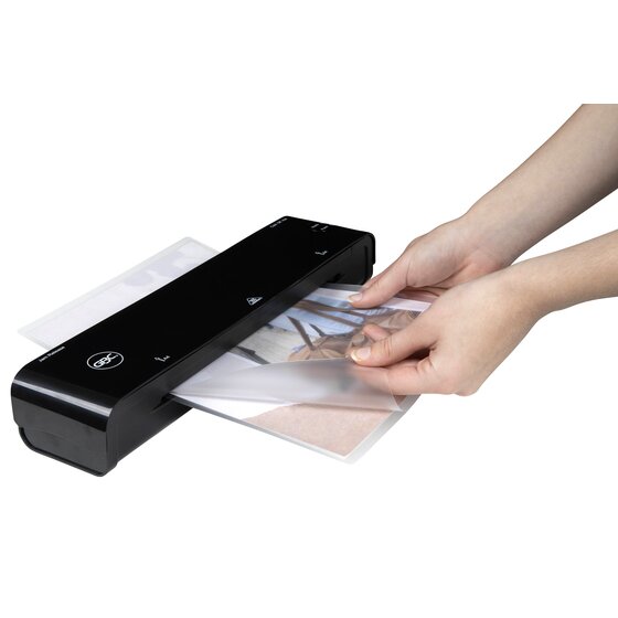 Hands feeding a laminated photo into a black GBC pouch laminator, shown to illustrate use; the laminator is sold separately