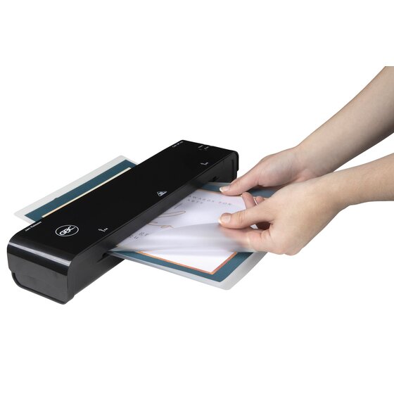 Hands feeding a laminated sheet into a black GBC pouch laminator, shown to illustrate use; the laminator is sold separately