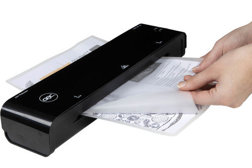 Hand pulling a laminated A4 page from the output side of a black GBC pouch laminator on a plain white background