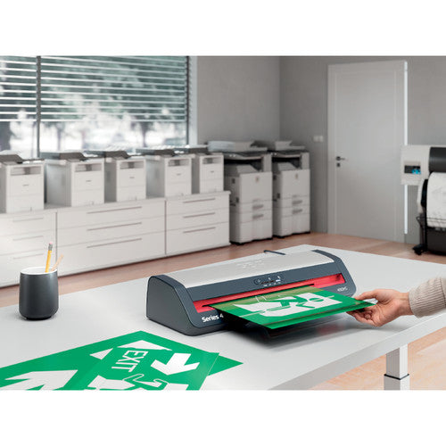 GBC 480HS on an office desk as a hand feeds a green exit sign through it, with copiers and cabinets in the background