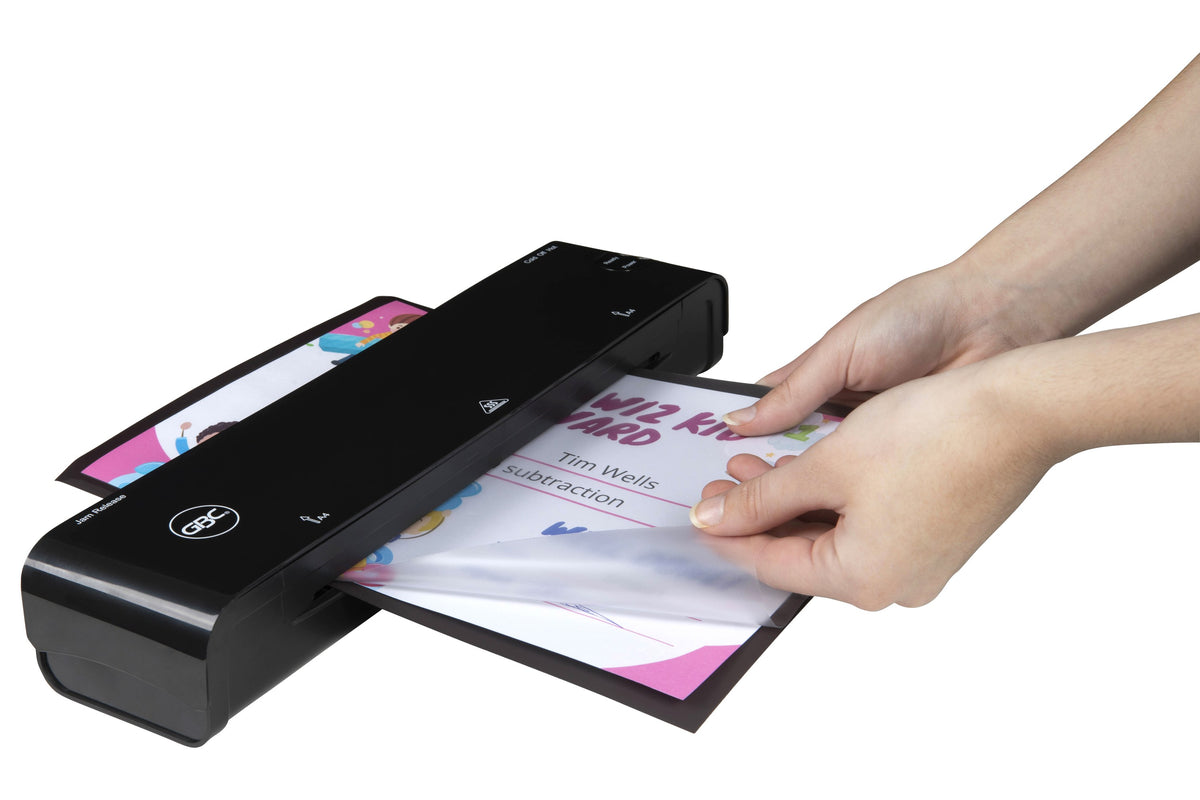 Two hands feeding a GBC A4 magnetic back pouch with a dark backing sheet and a printed class award into a black GBC pouch laminator
