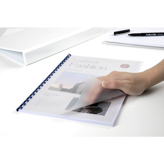 Hand lifting a frosted front cover on a comb bound fashion lookbook lying on a white desk beside a pen