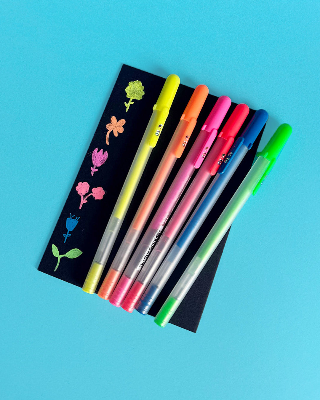 Six fluorescent Moonlight pens beside flower doodles drawn on a black bookmark