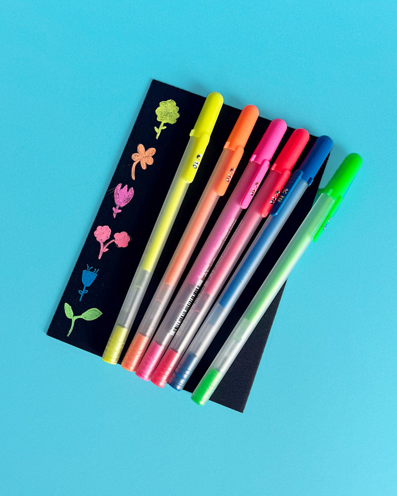 Six fluorescent Moonlight pens beside flower doodles drawn on a black bookmark