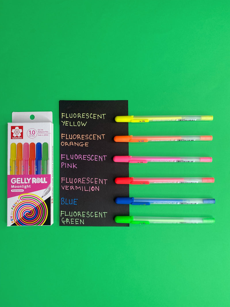 Moonlight Fluorescent box and six pens beside a black colour sample card on green