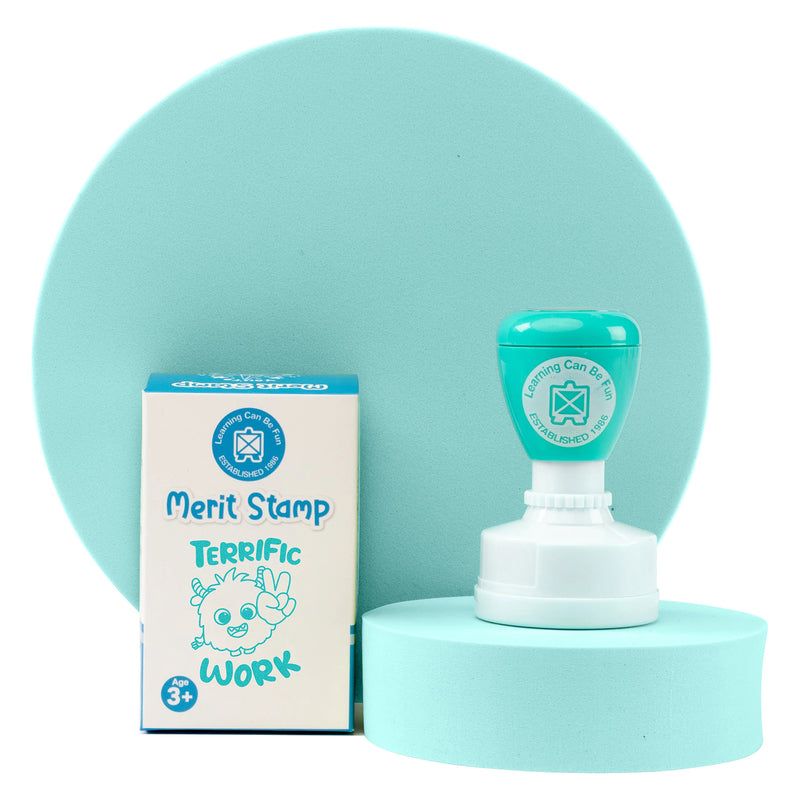 Retail packaging and self inking Terrific Work merit stamp displayed against a soft teal presentation backdrop. The packaging highlights the positive reward theme while showcasing the compact stamp designed for everyday educational use.