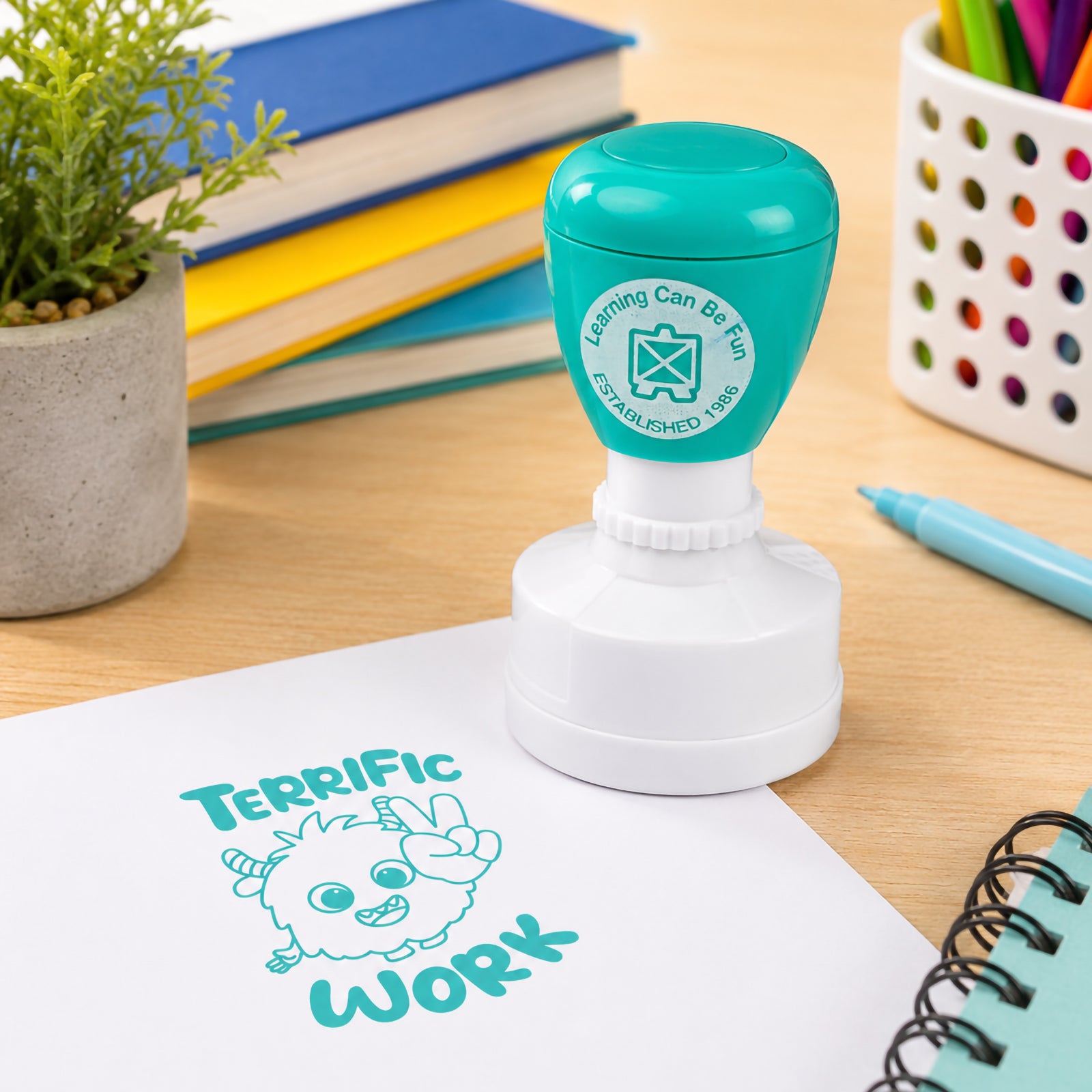 Learning Can Be Fun Terrific Work reward stamp positioned on a worksheet surrounded by books, classroom supplies and learning materials. The bright teal impression showcases the motivational message and playful character designed to encourage students and celebrate success.