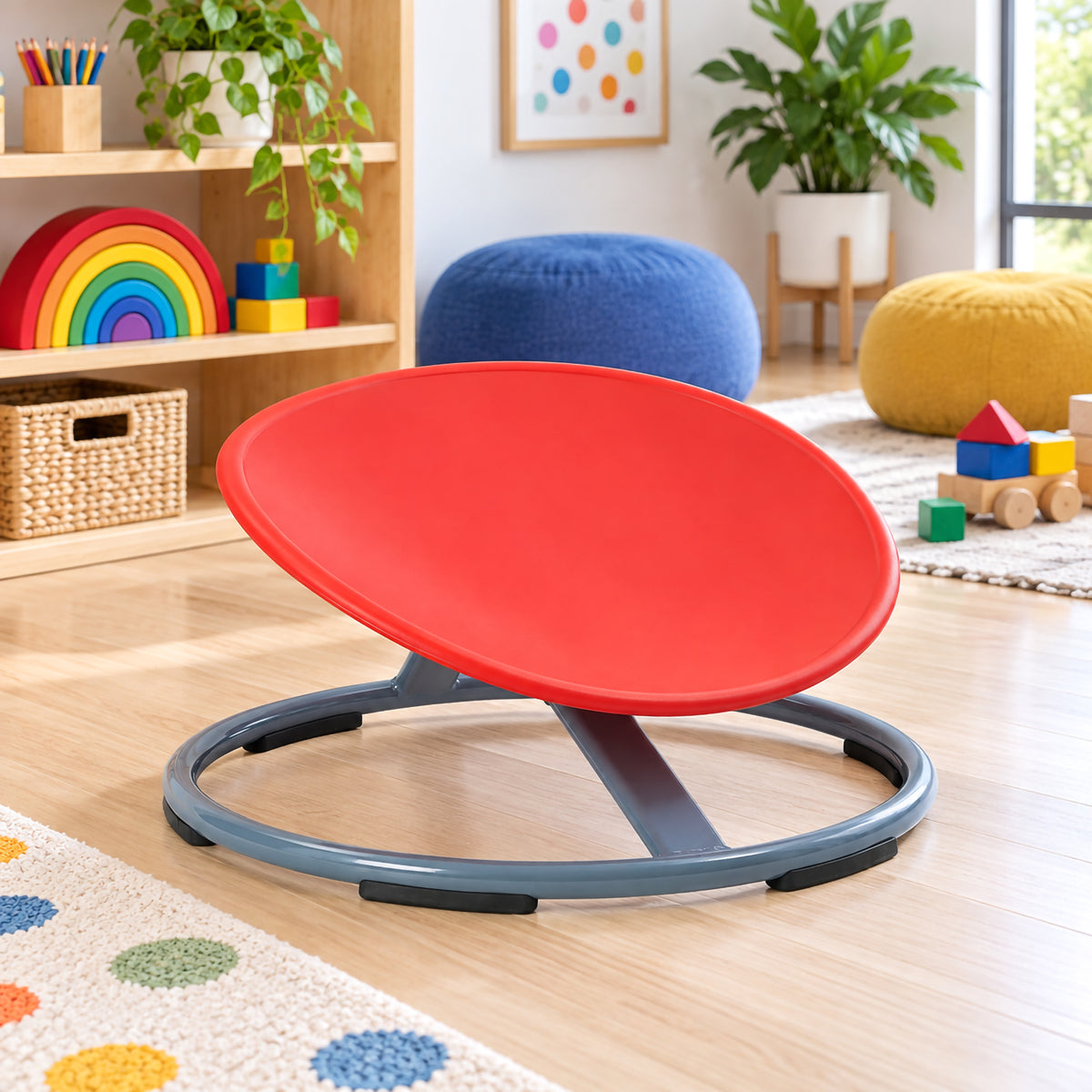 Gonge Balance Disc shown without a user in a bright classroom setting, highlighting the angled red seat and low circular grey metal base. The open construction, support structure and rubber contact points are clearly visible, presenting the spinning seat as an engaging addition to supervised balance, coordination and physical development activities.