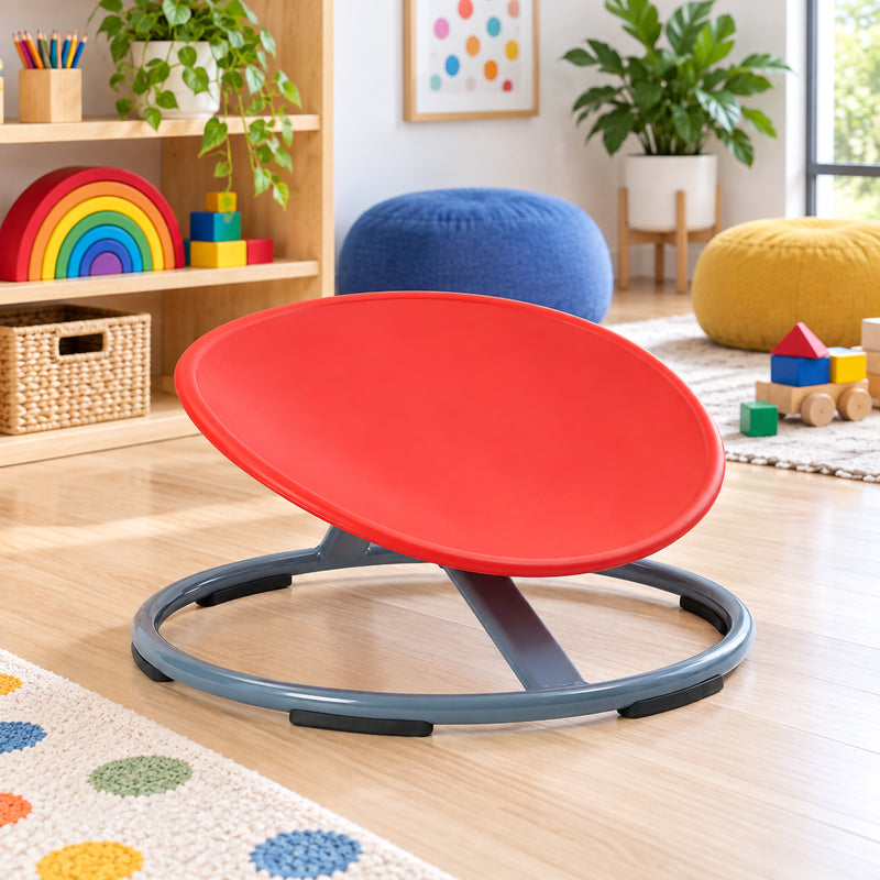 Gonge Balance Disc shown without a user in a bright classroom setting, highlighting the angled red seat and low circular grey metal base. The open construction, support structure and rubber contact points are clearly visible, presenting the spinning seat as an engaging addition to supervised balance, coordination and physical development activities.