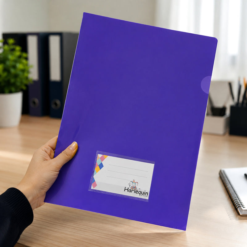 A person holds a Harlequin purple letter file featuring a clear card pocket on the front for labelling. The file is displayed in a modern office workspace with a timber desk, stationery, binders and soft natural lighting, demonstrating comfortable handling and everyday office use.