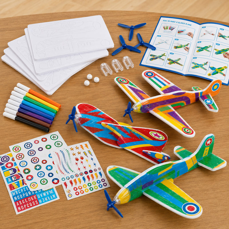 Three completed glider planes with unique colourful designs are displayed alongside markers, stickers, propellers, nose weights and assembly instructions. The image showcases the finished results and included craft components.