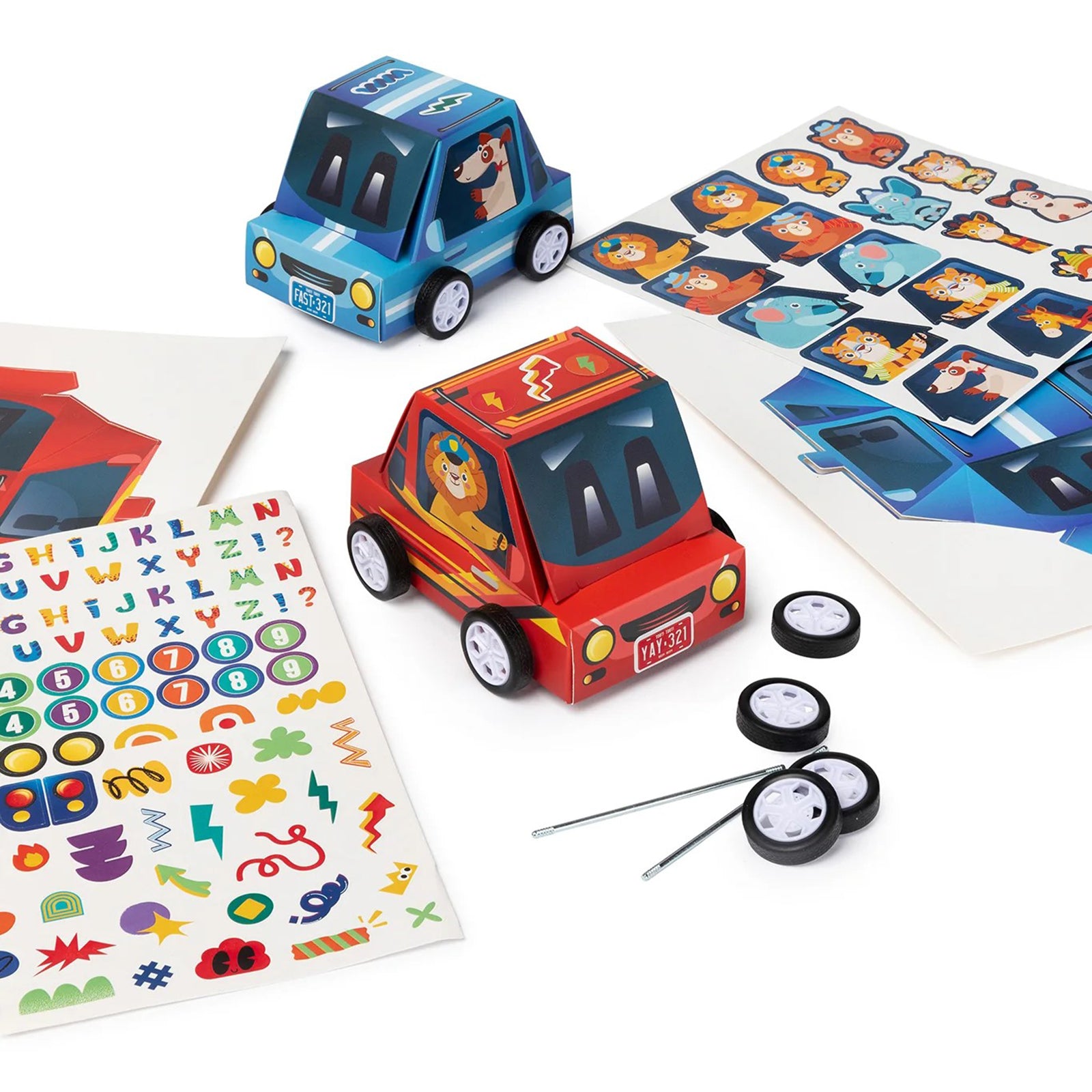 Completed red and blue racing cars displayed alongside character stickers, vehicle templates, wheels and axle components. The arrangement highlights the creative play and decoration possibilities included in the kit.