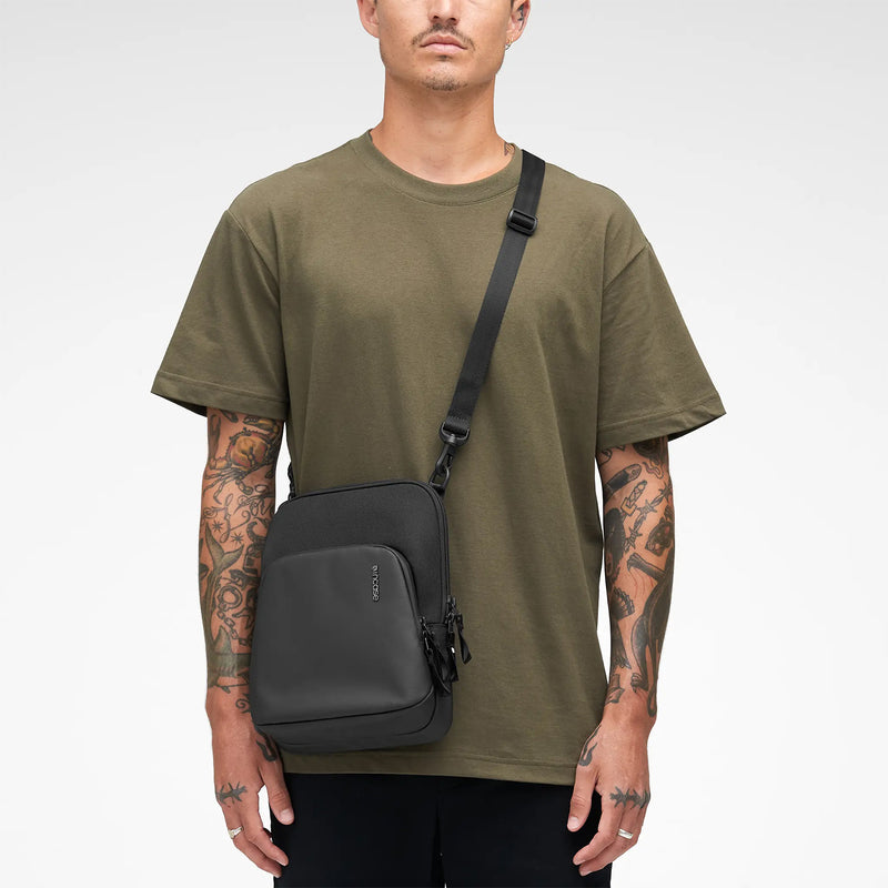 Studio portrait showing the Incase A.R.C. Crossbody Bag worn crossbody with casual clothing. The image focuses on the streamlined silhouette, premium materials and balanced proportions, demonstrating its versatile unisex design suitable for work, travel and everyday city life.