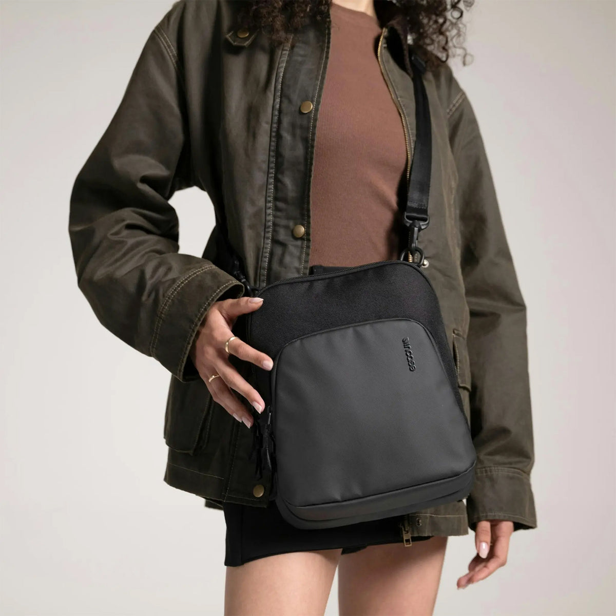 Lifestyle image featuring the Incase A.R.C. Crossbody Bag worn with casual outerwear, highlighting the modern minimalist aesthetic and practical everyday functionality. The comfortable crossbody design, premium recycled materials and compact storage make it ideal for carrying tablets, phones and daily essentials in style.