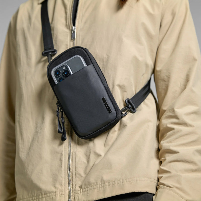 Front lifestyle view showing the compact Incase crossbody bag worn securely against a casual jacket. The visible phone placement demonstrates quick access while maintaining a streamlined appearance.