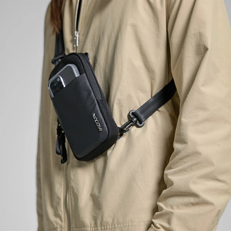 Angled lifestyle close up displaying the bag worn across the body with a smartphone visible in the front pocket. The image highlights the clean styling and easy access storage while walking or commuting.