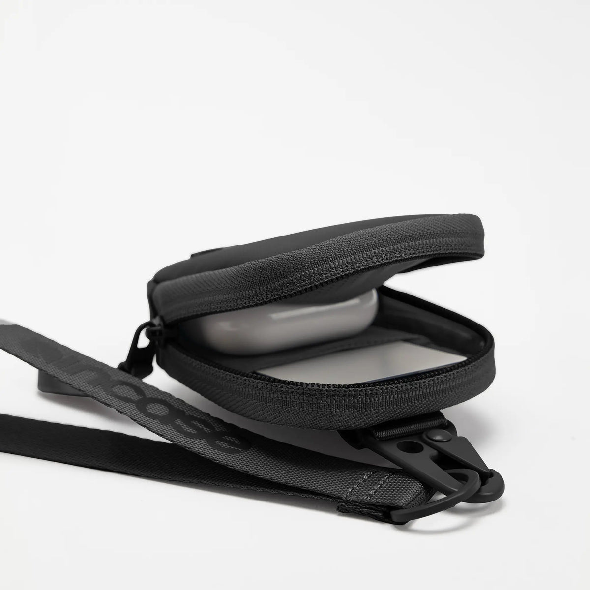 Black A.R.C. Compact Pouch unzipped to show an AirPods case inside, with the wrist strap attached