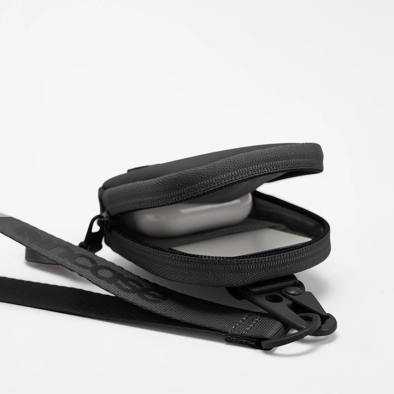 Black A.R.C. Compact Pouch unzipped to show an AirPods case inside, with the wrist strap attached