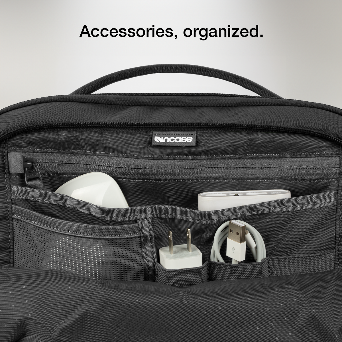 Close-up of the open organiser pocket of the black Incase A.R.C. Daypack with a charger and cables, with Incase's caption on organised accessories