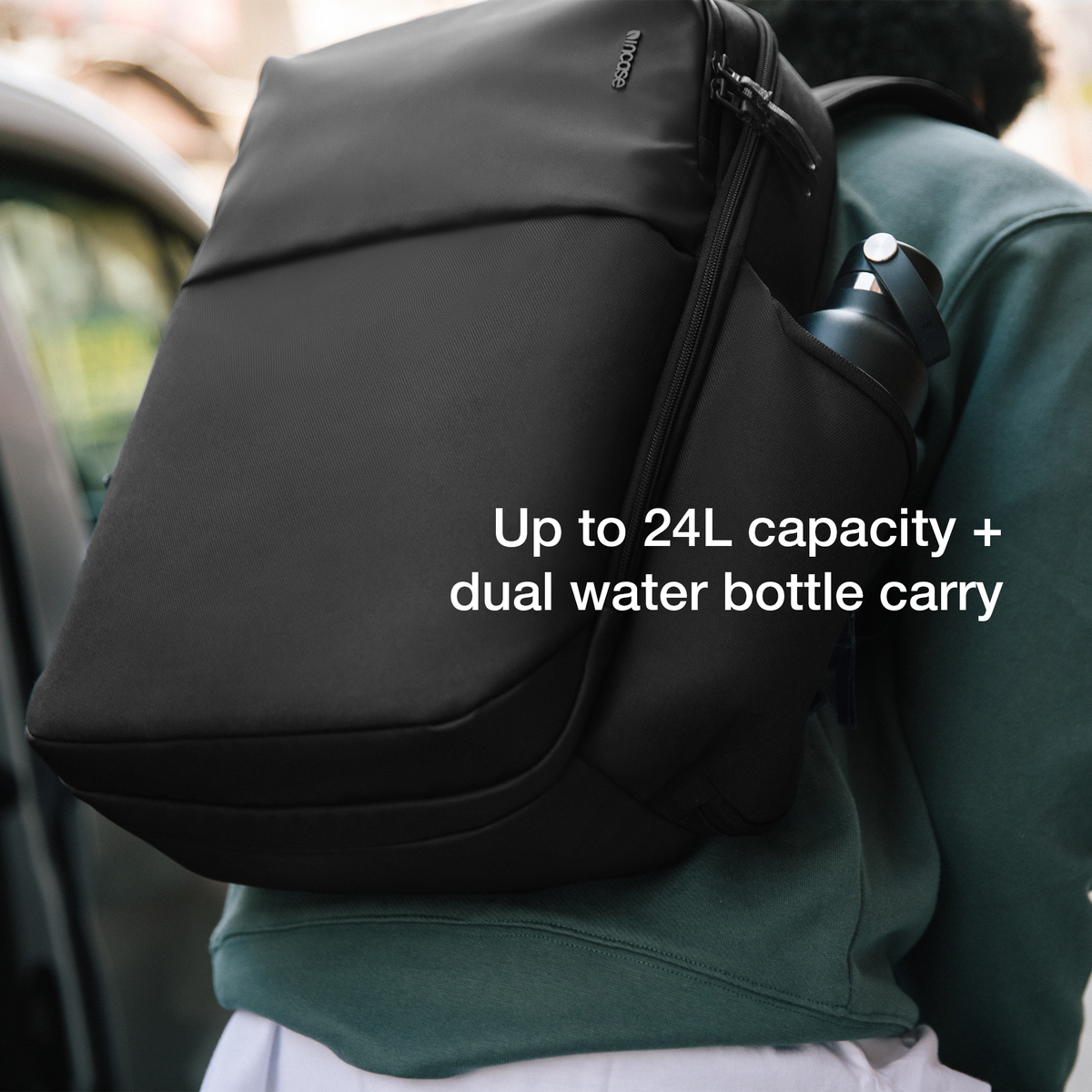 Black Incase A.R.C. Daypack worn on one shoulder with a water bottle in the side pocket, captioned Up to 24L capacity plus dual water bottle carry