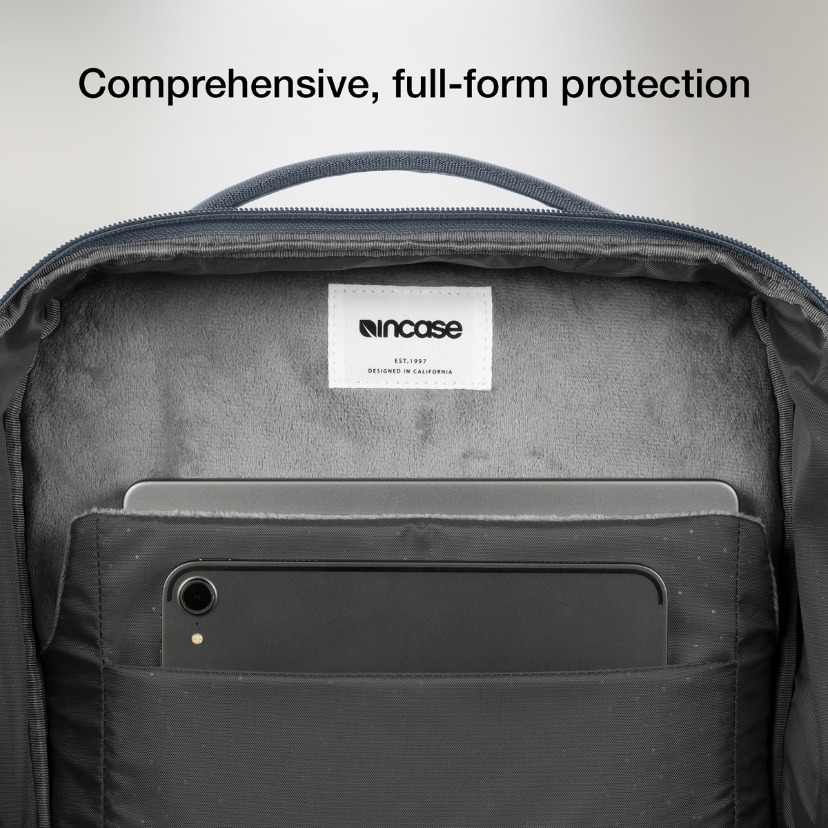 Open laptop compartment of the navy Incase A.R.C. Daypack, showing the soft grey lining and a tablet in the front slip pocket