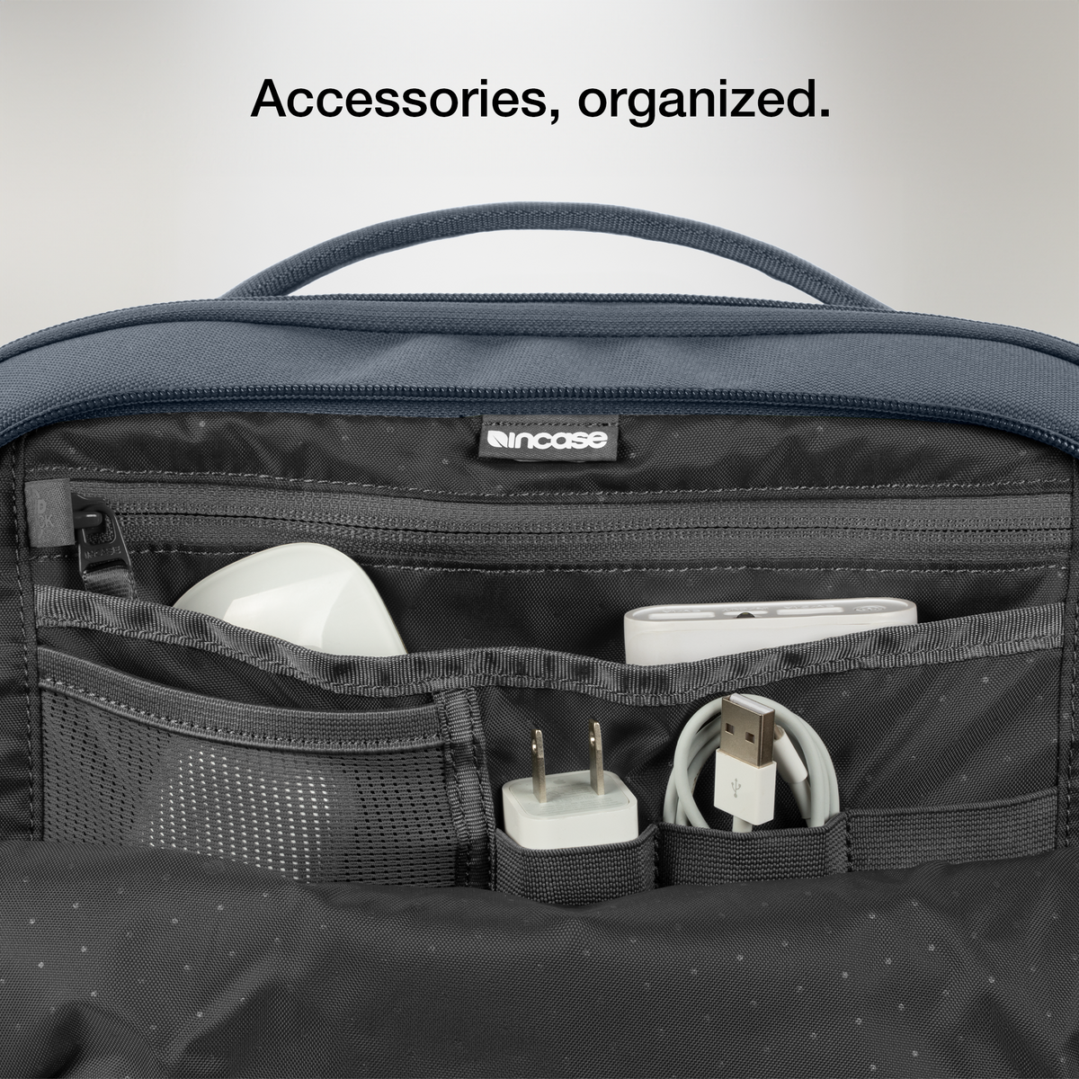 Close-up of the open organiser pocket of the navy Incase A.R.C. Daypack with a charger and cables, with Incase's caption on organised accessories