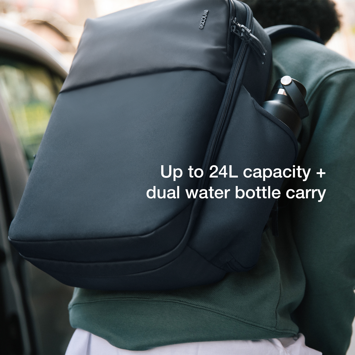 Navy Incase A.R.C. Daypack worn on one shoulder with a water bottle in the side pocket, captioned Up to 24L capacity plus dual water bottle carry