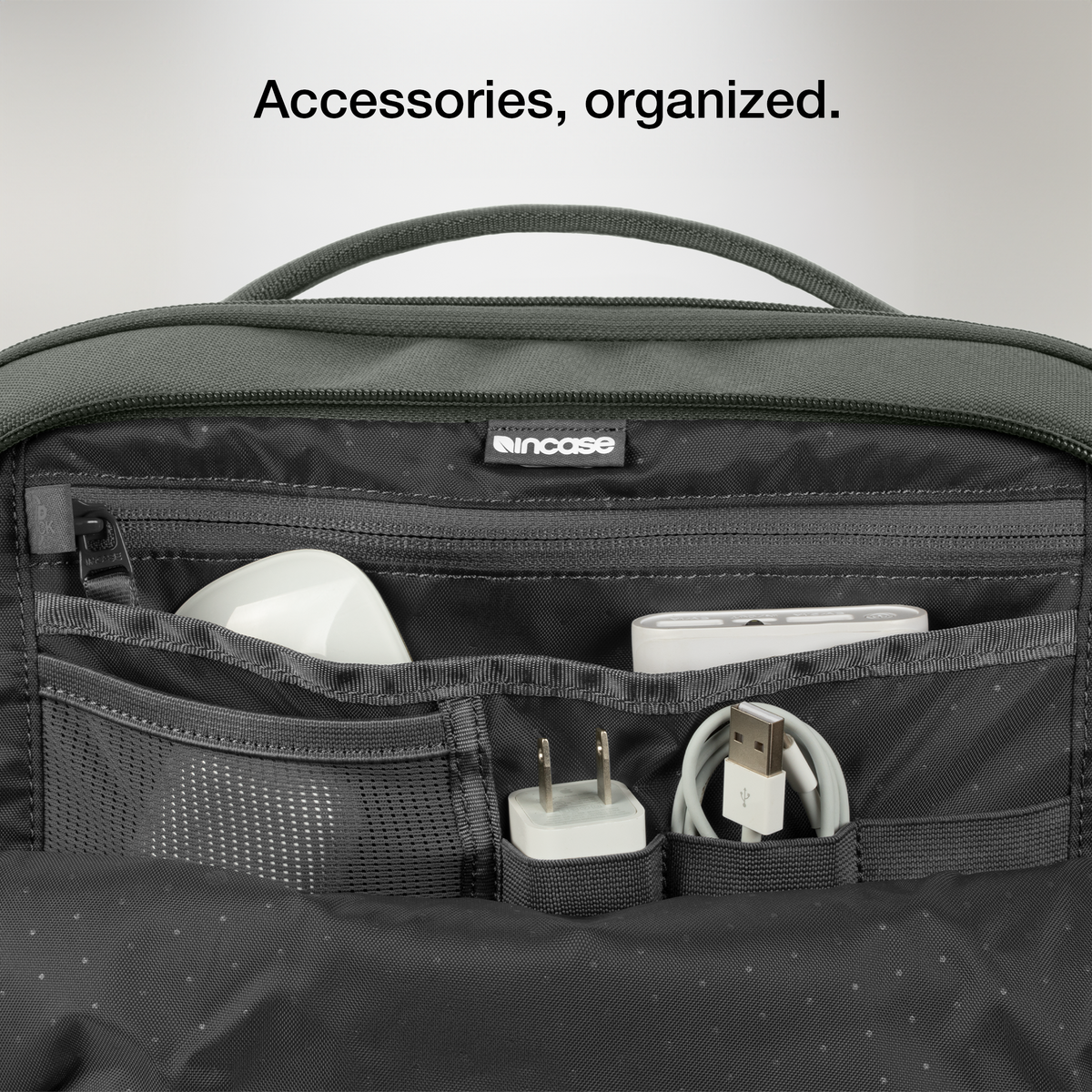 Close-up of the open organiser pocket of the Smoked Ivy Incase A.R.C. Daypack with a charger and cables, with Incase's caption on organised accessories