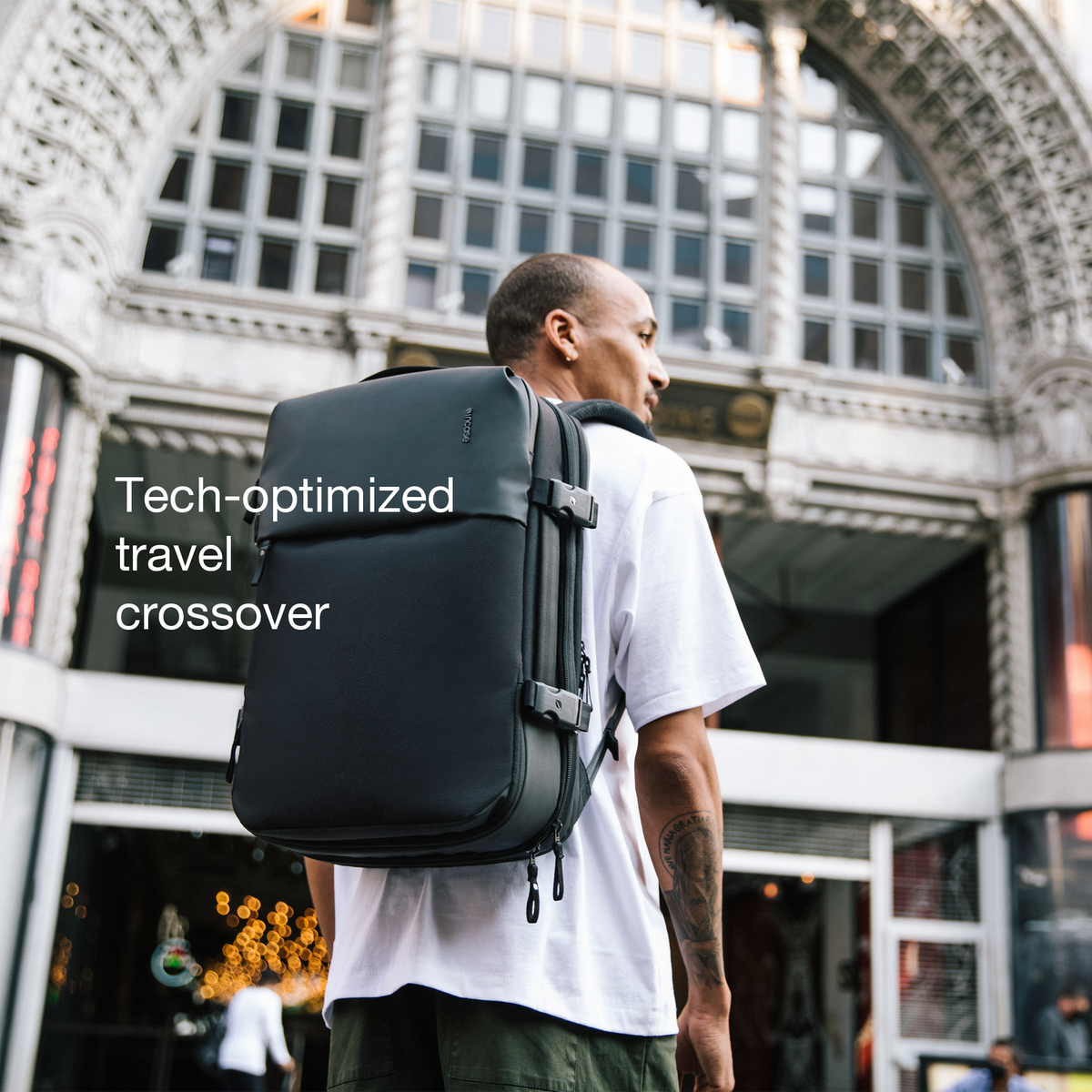 Model wearing the navy Incase A.R.C. Travel Pack outside a building, with Incase's caption describing a tech-optimised travel crossover