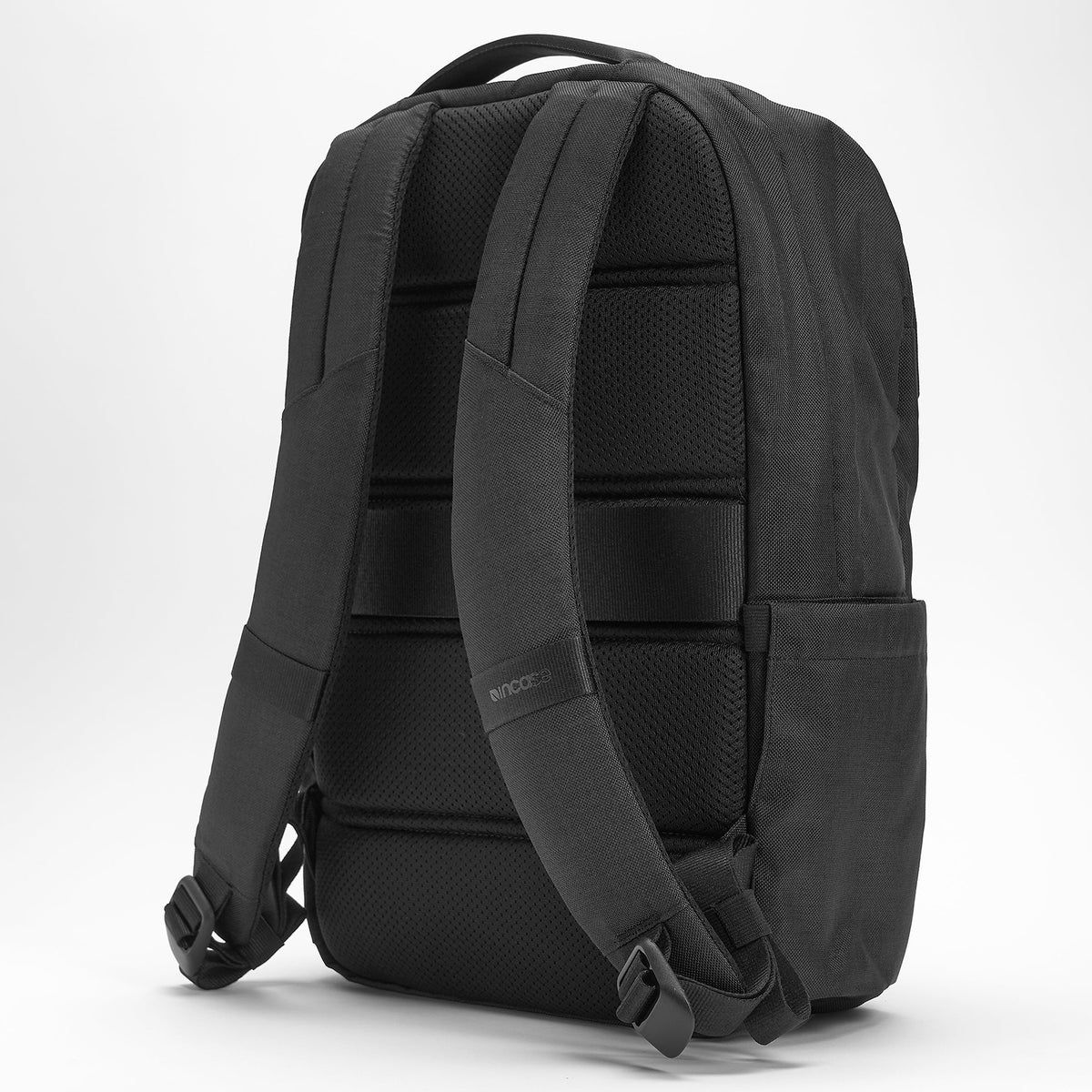 Rear angled product view illustrating the ergonomic shoulder straps, padded back construction and side profile while maintaining a clean minimalist aesthetic.