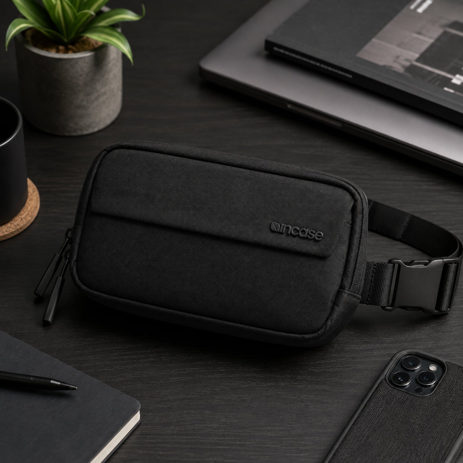 Office desktop lifestyle scene featuring the Incase Crosstown Sling Black positioned beside a notebook, laptop, coffee mug and smartphone. The refined appearance complements professional workspaces while showcasing its premium materials.