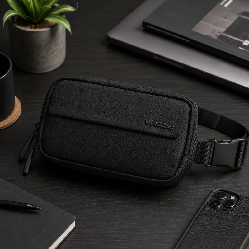 Office desktop lifestyle scene featuring the Incase Crosstown Sling Black positioned beside a notebook, laptop, coffee mug and smartphone. The refined appearance complements professional workspaces while showcasing its premium materials.