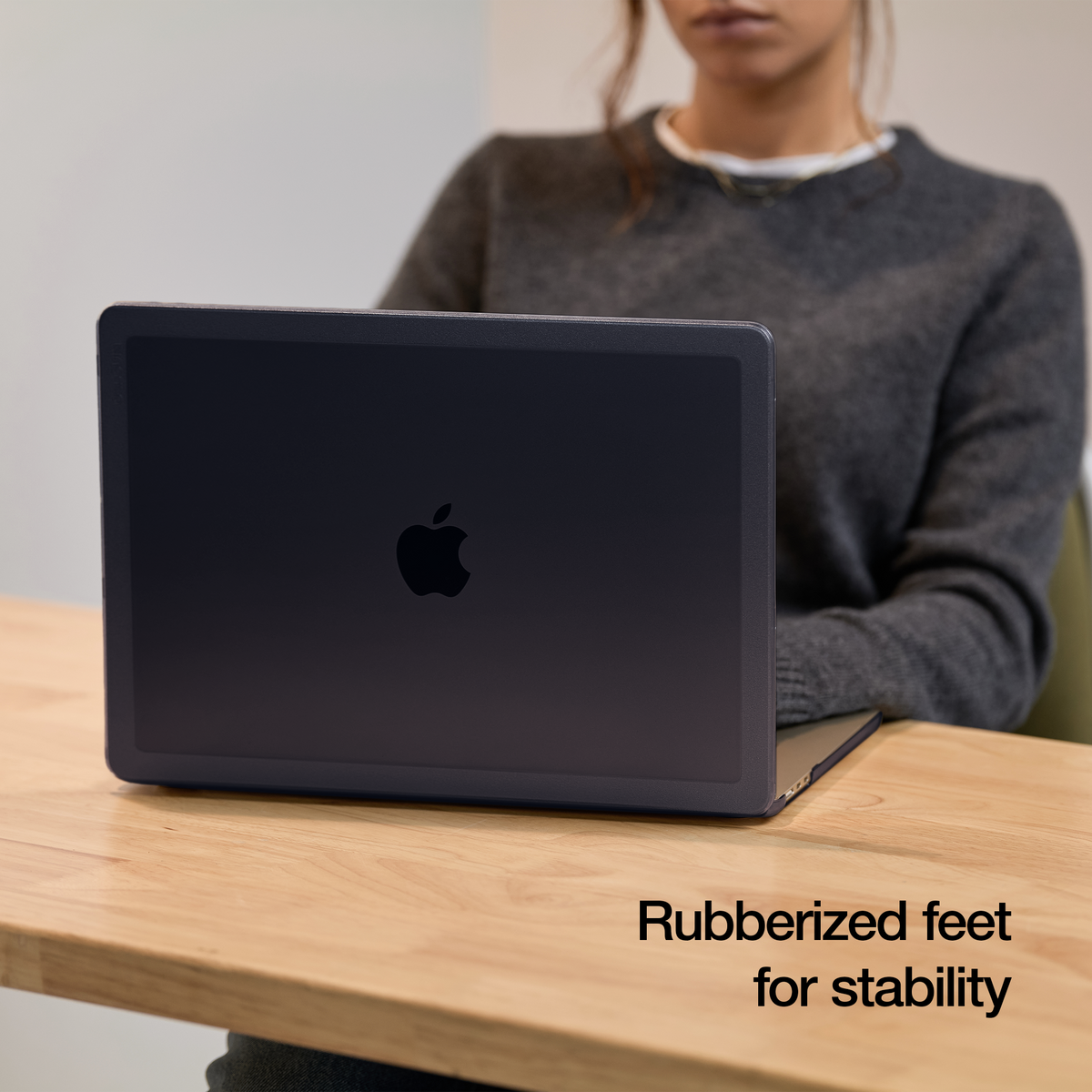 Dark blue MacBook Air in the Black Edge Hardshell open on a wooden desk, with the laptop colour showing through the tinted shell and the overlay text Rubberized feet for stability