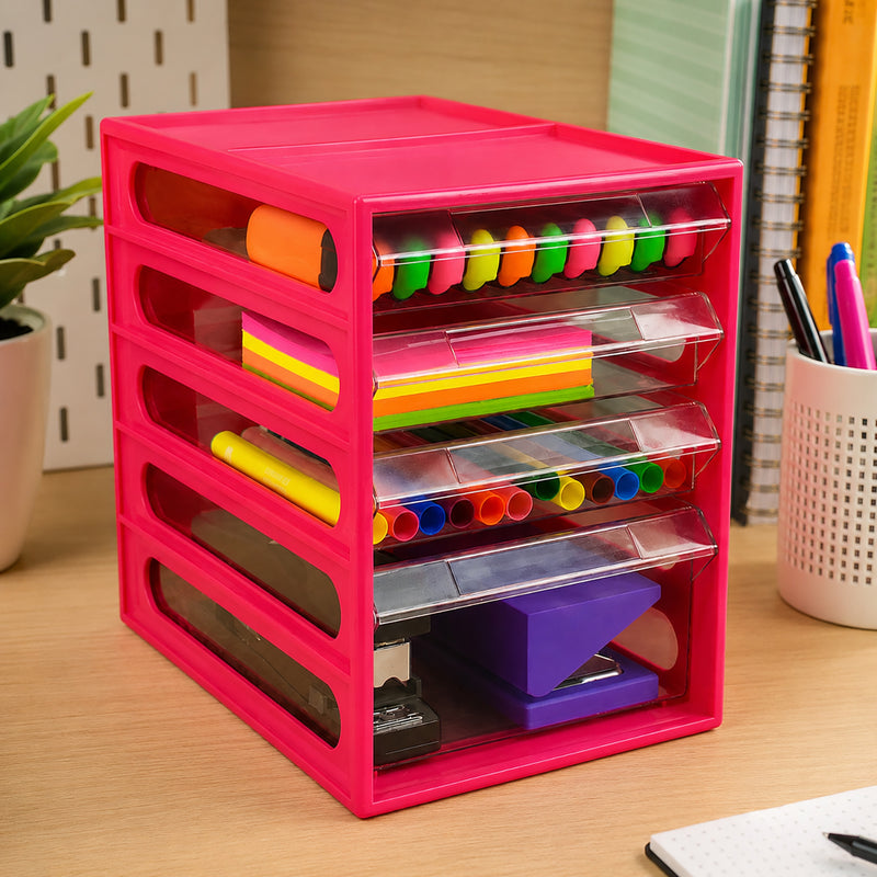 Angled view of the Italplast Watermelon Office Organiser positioned on a desk with books and stationery nearby. Three shallow clear drawers separate colourful writing and note taking supplies, while the deeper bottom drawer accommodates larger desktop equipment, demonstrating efficient vertical storage within a compact footprint.