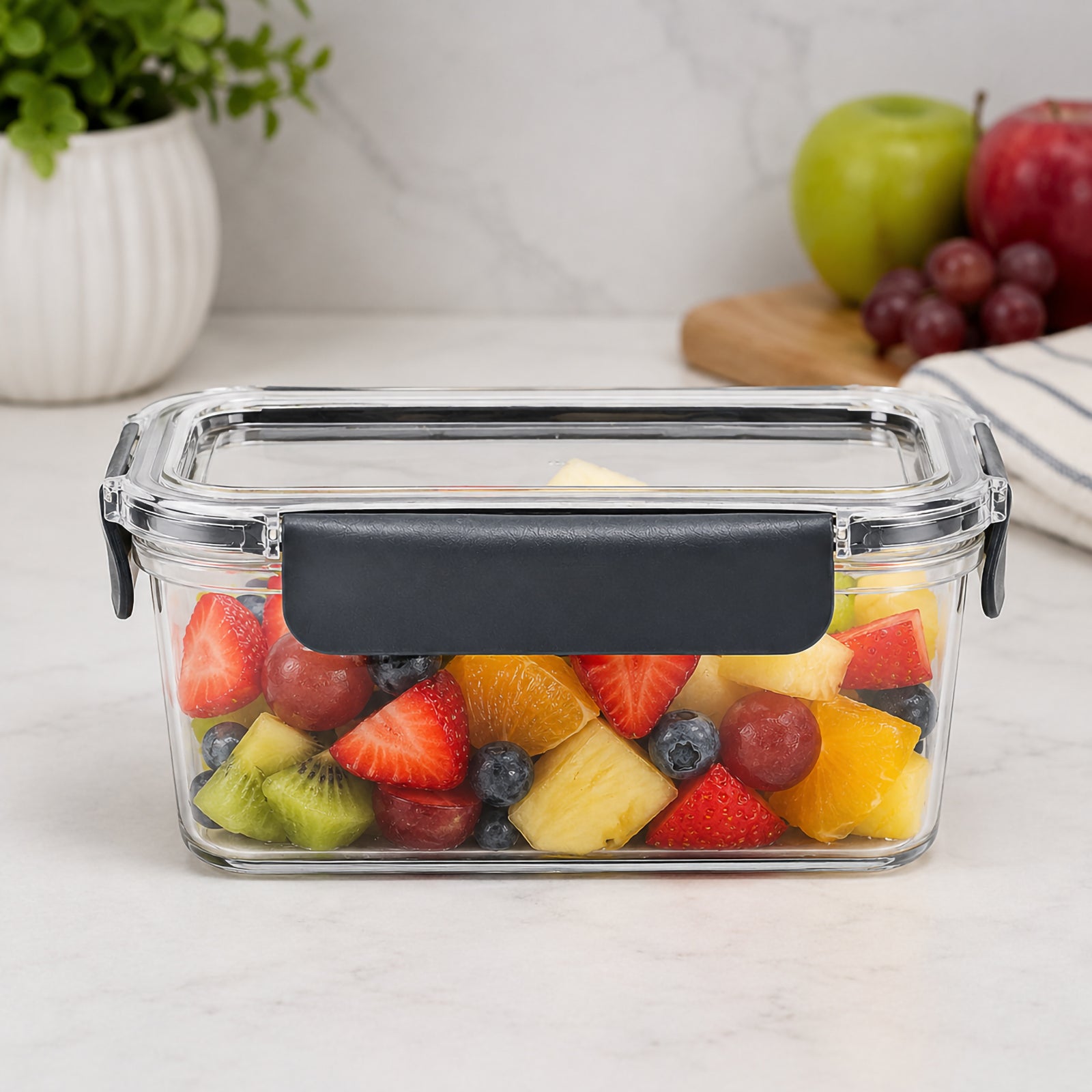 Front view of the Italplast 1.3 litre clear food container filled with colourful cut fruit including strawberries, grapes, kiwi, pineapple, orange and blueberries. The transparent container makes the contents clearly visible while the prominent dark front closure and matching side locks demonstrate its practical snap lock lid design for organised refrigerator food storage.