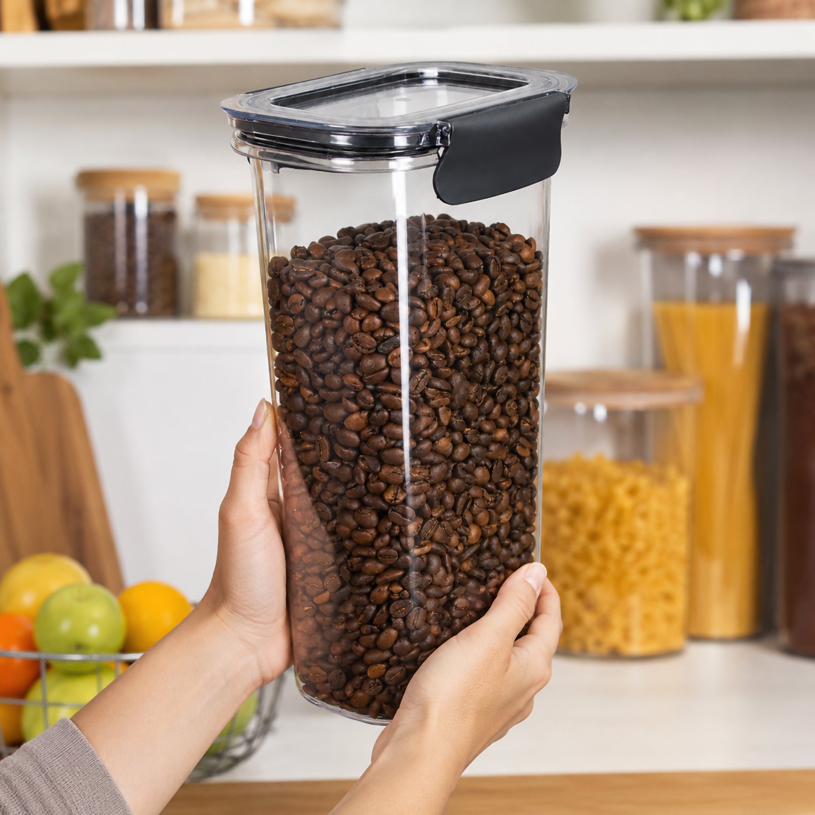 Italplast 1700ml clear Snap Lock Food Container held upright in both hands and filled with coffee beans in an organised kitchen pantry. The image demonstrates the containers tall, narrow proportions, transparent body and secure dark snap lock closures, showing a practical way to store coffee beans and other frequently used dry pantry ingredients.