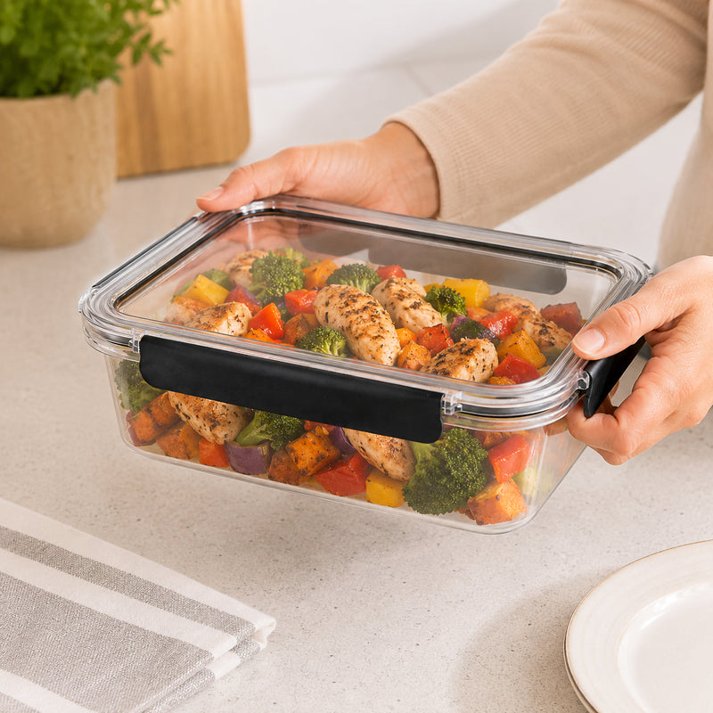 Italplast 2700ml clear Snap Lock Food Container held securely in both hands and filled with a prepared chicken and vegetable meal. The image highlights the generous rectangular capacity, transparent lid and body, and contrasting dark snap lock closures, demonstrating a practical option for meal preparation, leftovers and larger workplace lunches.