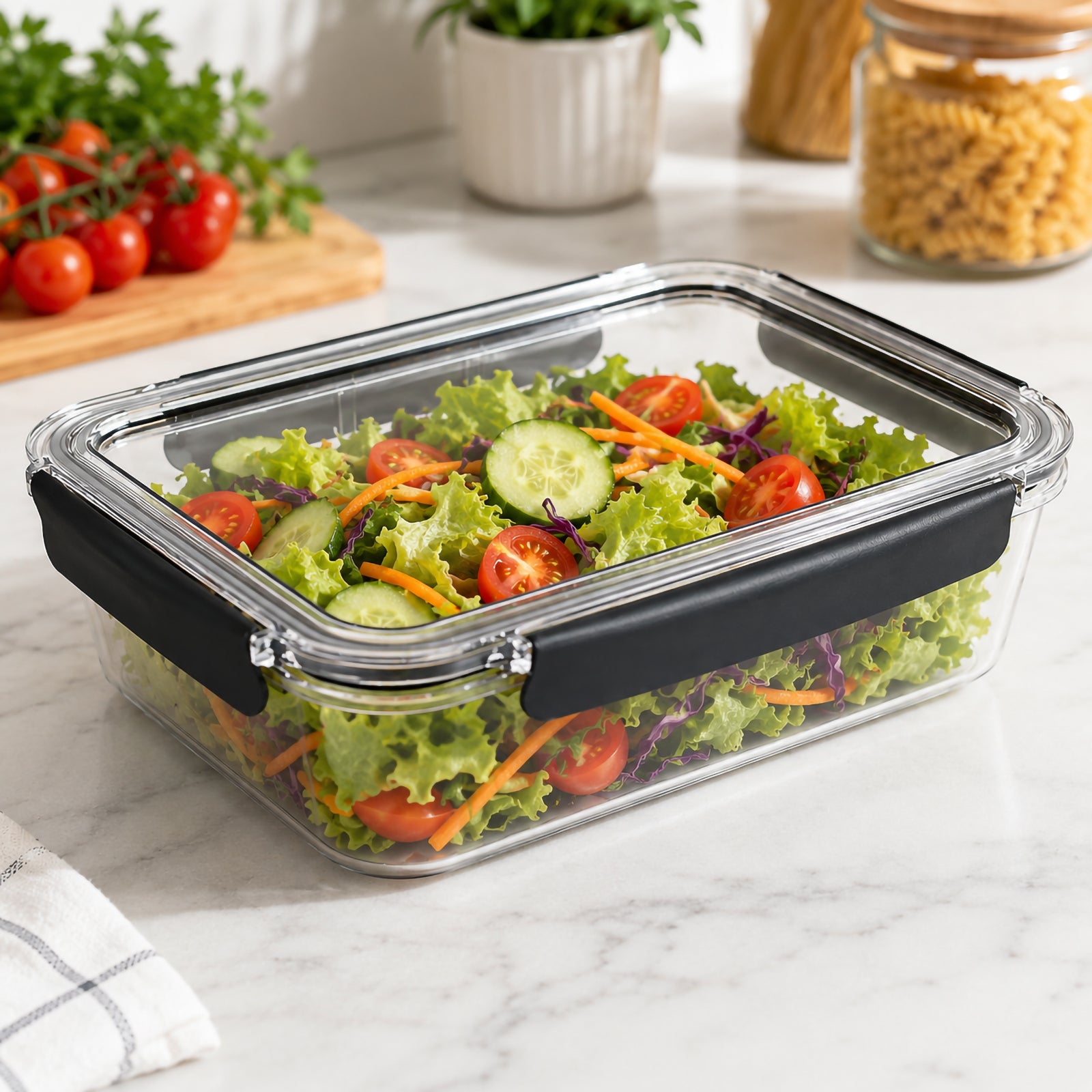 Angled kitchen view of the Italplast 2700ml Snap Lock Food Container filled with fresh salad ingredients including lettuce, cucumber and tomatoes. Its broad rectangular format offers useful space for larger salads and family portions, while clear walls and lid provide easy visibility and dark closures secure the container around its edges.