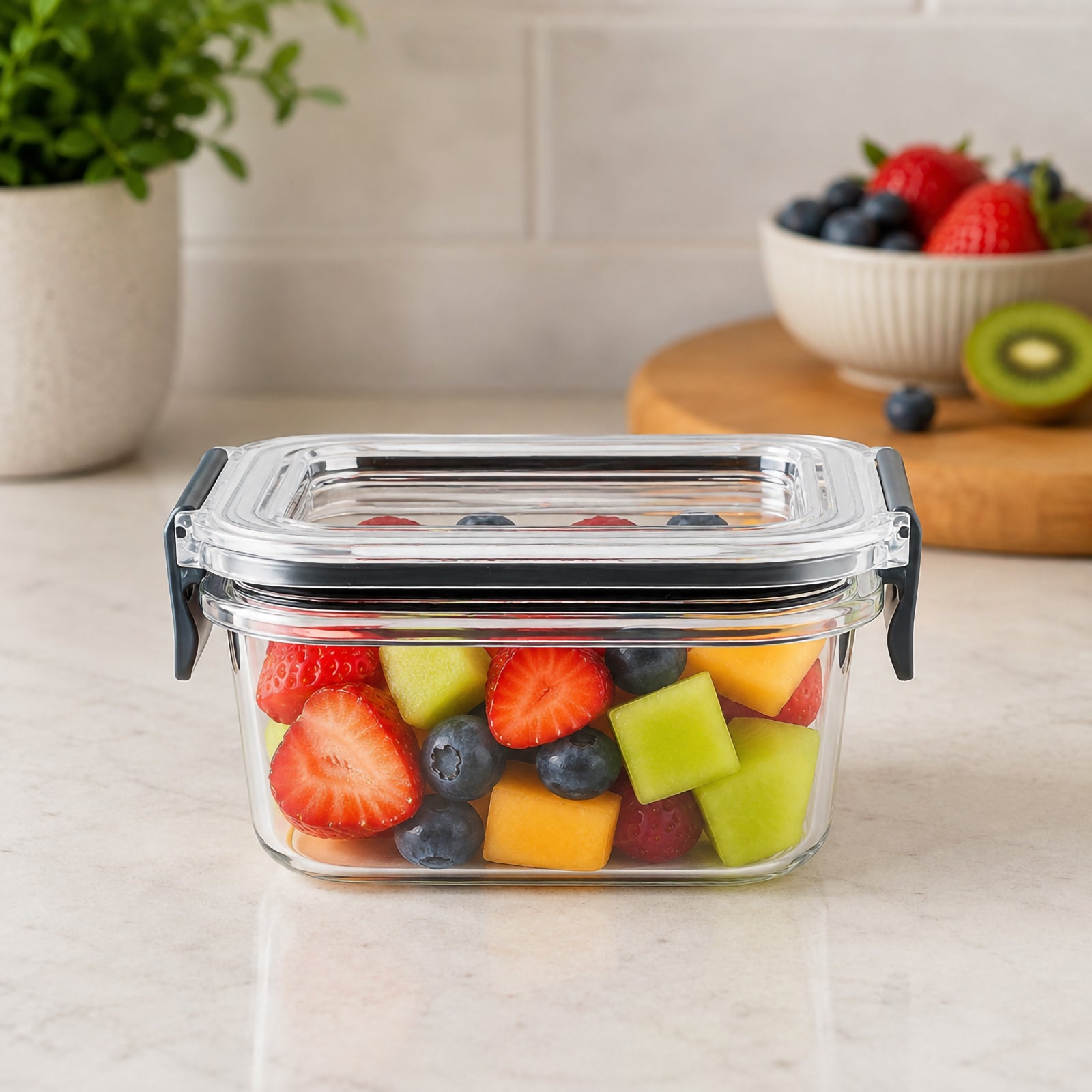 Front view of the Italplast 400ml clear food container filled with strawberries, blueberries and melon on a kitchen bench. Its compact rectangular shape, transparent lid and clear body make the contents easy to identify, while the dark locking tabs on each side highlight the secure snap lock closure designed for convenient food storage.