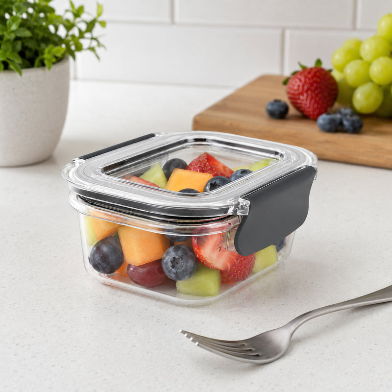 Angled view of the Italplast Snap Lock Food Container holding mixed fresh fruit beside a fork on a kitchen bench. The image highlights the clear construction, fitted lid and prominent dark snap lock closure, showing the practical 400ml size for individual snacks, prepared fruit, smaller servings and organised refrigerator storage.