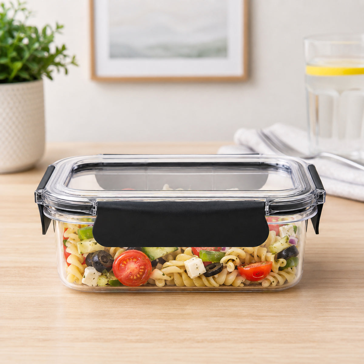 Front view of the Italplast 950ml clear food container filled with pasta salad on a timber surface. The low rectangular profile, transparent construction and broad black snap lock closure are clearly visible, showing how the container keeps prepared meals easy to identify while providing compact storage for everyday lunches and leftovers.